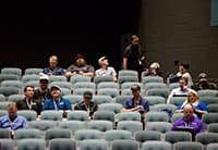 A small group of people wearing lanyards sit scattered across mostly empty rows of seats in the auditorium at the UEN Tech Summit, some engaged in conversation while others look toward the front.
