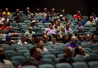 A group of people sit scattered throughout rows of seats in a dimly lit auditorium at the UEN Tech Summit, attentively facing the front.